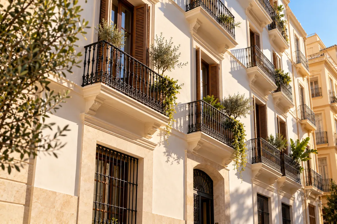 Edificio de apartamentos rehabilitado en Málaga, con fachada de cal clara, zócalo de piedra y ático con pérgola de lamas