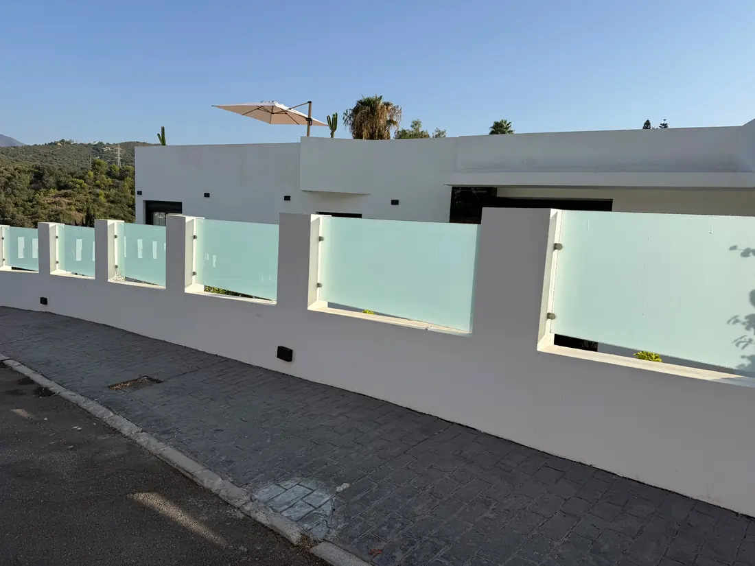 Muro de parcela blanco con paños de vidrio translúcido visto desde la calle en una villa